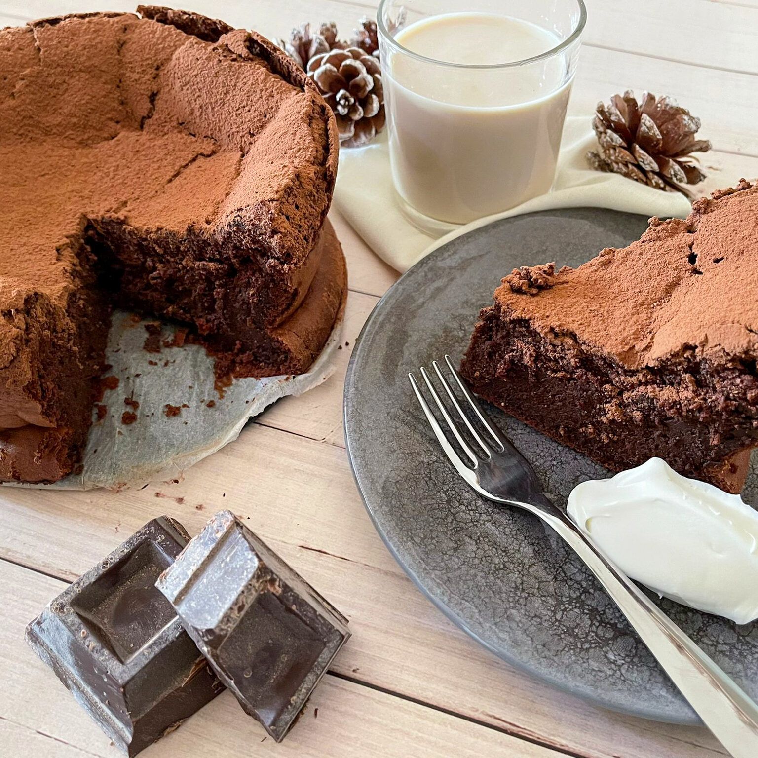 Una torta al cioccolato con una fetta staccata si trova su un piatto accanto a un bicchiere di latte.