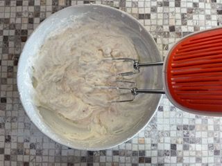 Un mixer rosso è appoggiato accanto a una ciotola di pastella.