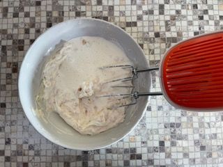 Un mixer rosso è appoggiato accanto a una ciotola di pastella.