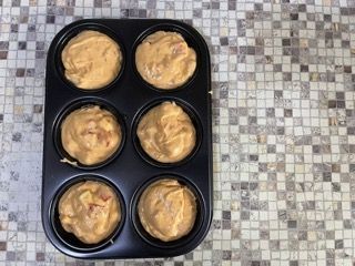 Uno stampo per muffin pieno di impasto è appoggiato su un tavolo piastrellato.