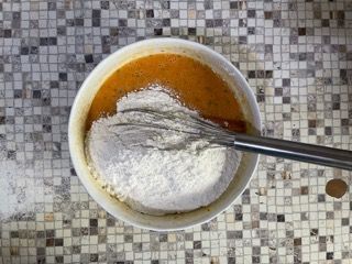 Una ciotola di pastella con farina e una frusta dentro.