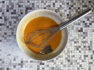 Una ciotola di salsa con una frusta dentro su un tavolo piastrellato.