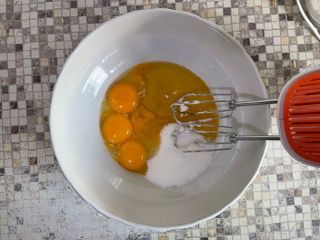 Una ciotola bianca piena di uova e zucchero accanto a una planetaria.