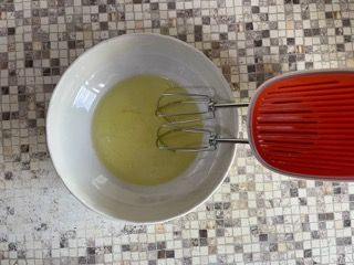 Una ciotola di liquido accanto a un mixer su un bancone piastrellato.