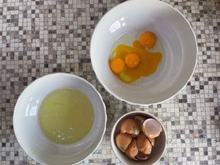 Tre ciotole di uova e una ciotola di uova rotte su un tavolo.