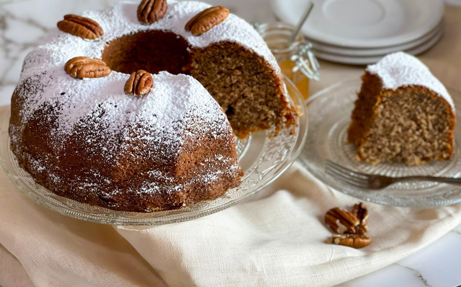 Un ciambellone con noci pecan e zucchero a velo sopra è su un piatto di vetro.