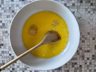 Una ciotola di liquido giallo con un cucchiaio di legno dentro.