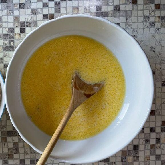 Una ciotola di liquido giallo con un cucchiaio di legno dentro