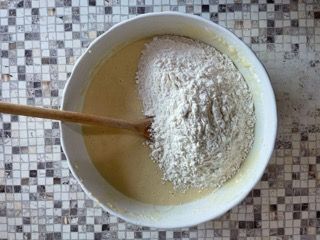 Una ciotola di pastella con farina e un cucchiaio di legno dentro.