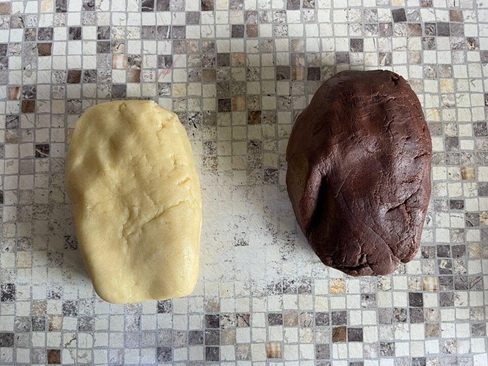 Due palline di pasta, una gialla e una marrone, sono appoggiate su un bancone piastrellato.