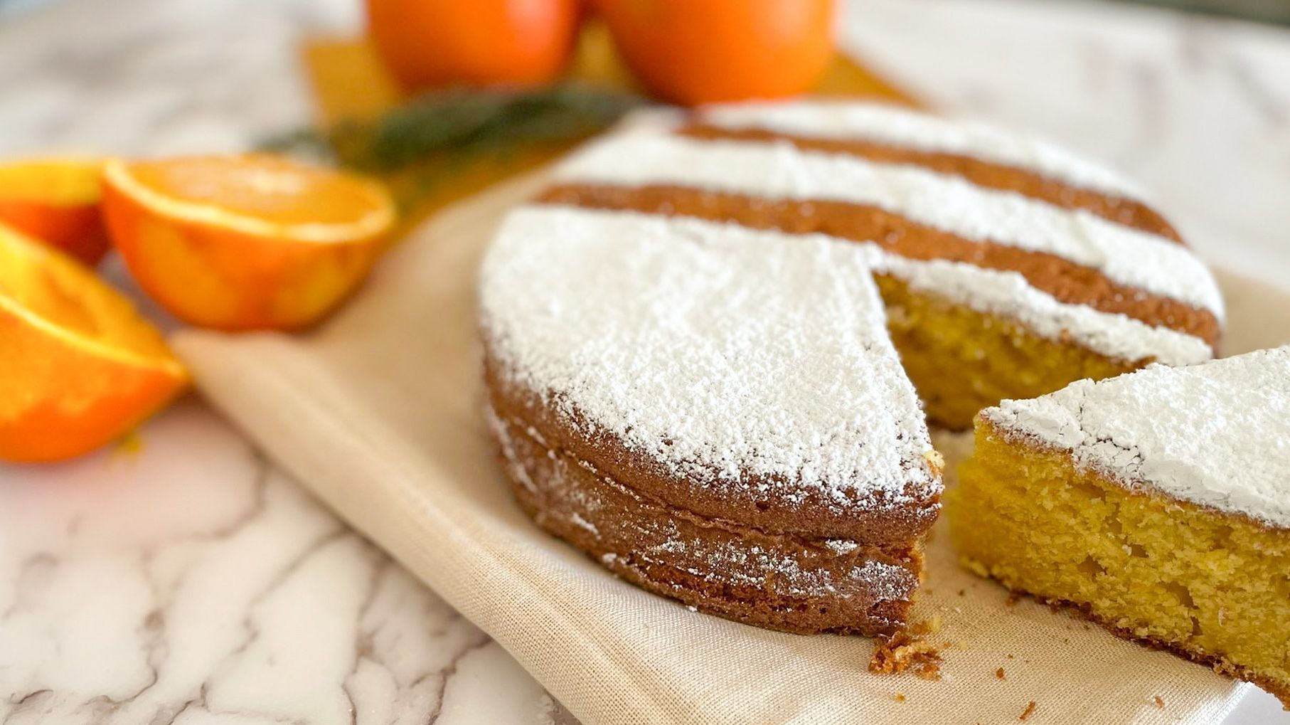Una torta ricoperta di zucchero a velo è appoggiata su un tagliere di legno.