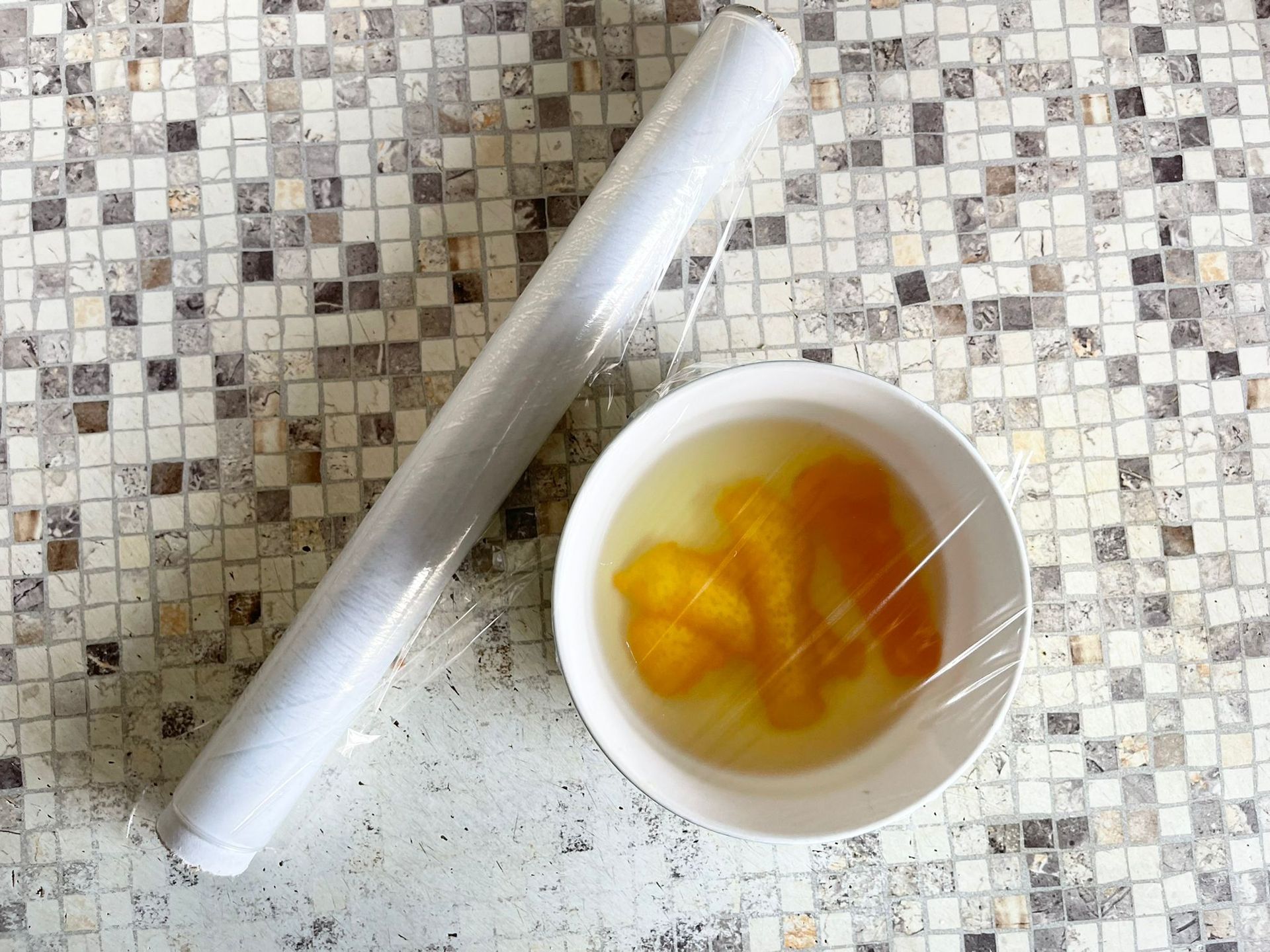 Una ciotola di cibo è avvolta in pellicola trasparente accanto a un rotolo di pellicola trasparente.