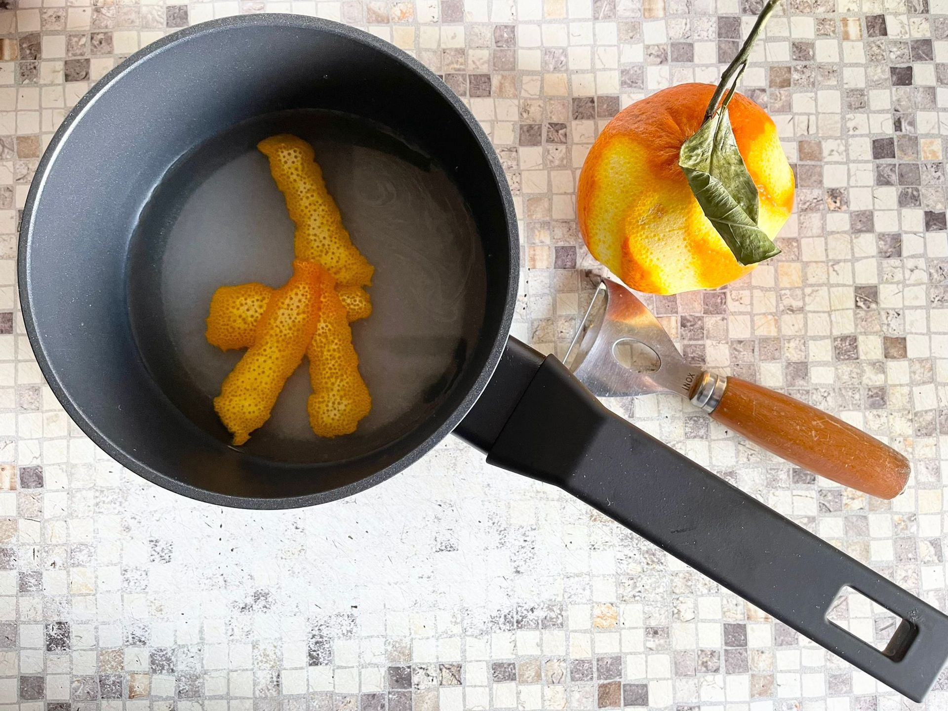 Una pentola d'acqua con dentro delle arance sbucciate.