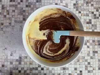 Una ciotola di impasto per torta al cioccolato con una spatola dentro.