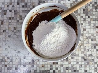 Una ciotola di impasto al cioccolato con farina e una spatola dentro.