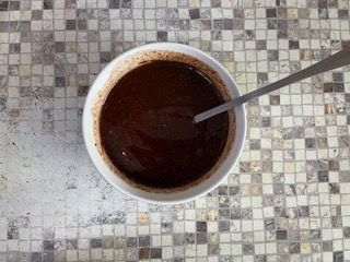 Una ciotola di salsa al cioccolato con un cucchiaio dentro su un tavolo a scacchi.