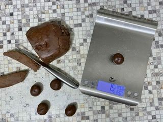 Una bilancia in acciaio inossidabile è appoggiata su un tavolo accanto a un pezzo di impasto al cioccolato.