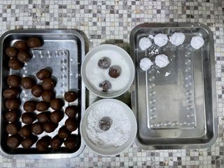 Un vassoio di palline di cioccolato accanto a due ciotole di zucchero a velo