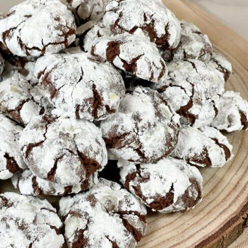 Una pila di biscotti al cioccolato ricoperti di zucchero a velo su un tagliere di legno.