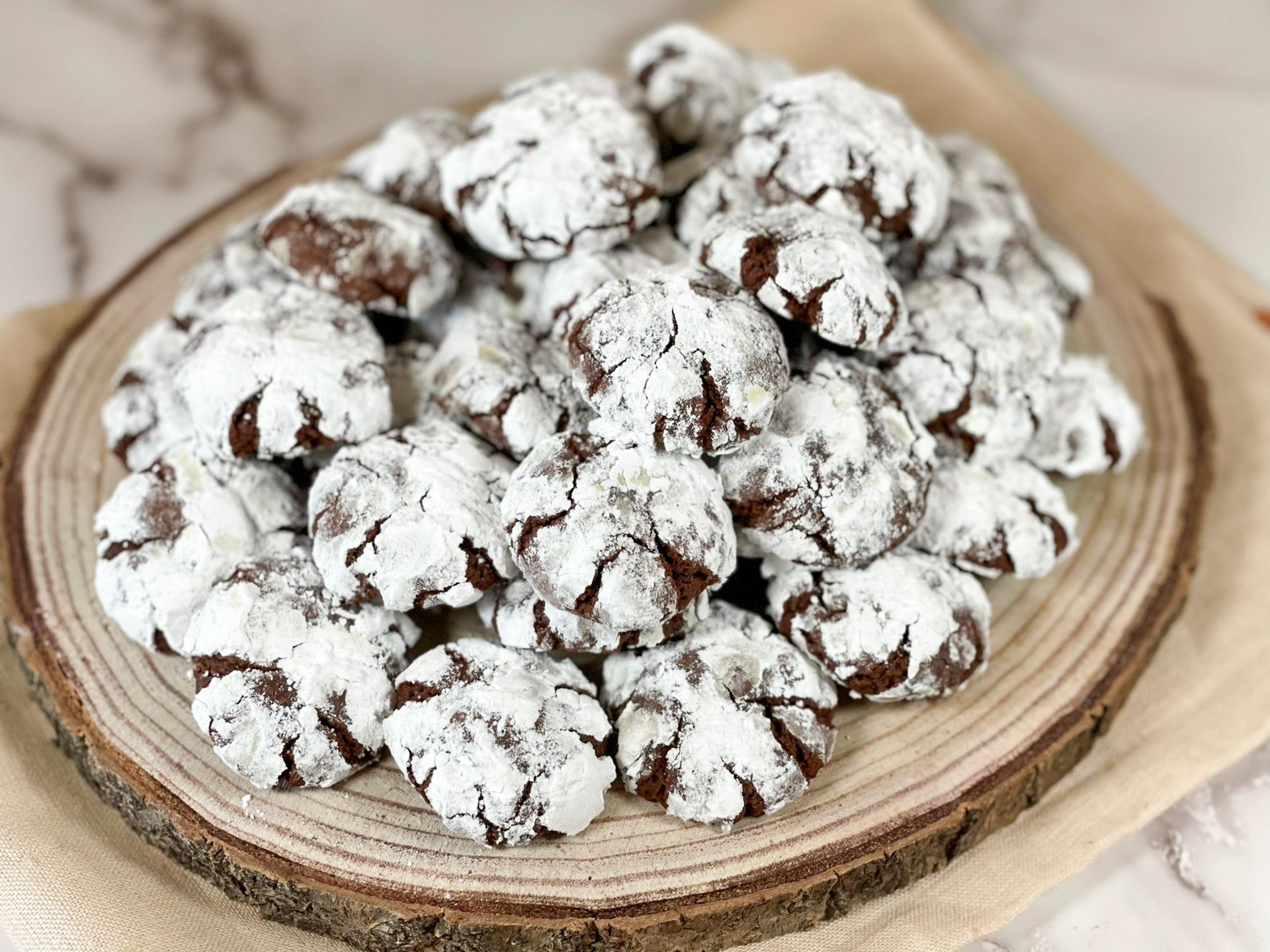 Una pila di biscotti al cioccolato ricoperti di zucchero a velo su un tagliere di legno.
