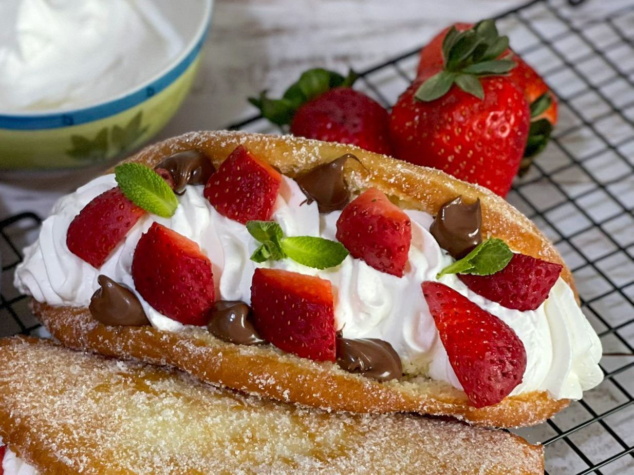Primo piano di un dessert con panna montata e fragole su una griglia di raffreddamento.