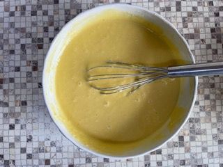 Una ciotola di liquido giallo con una frusta dentro.