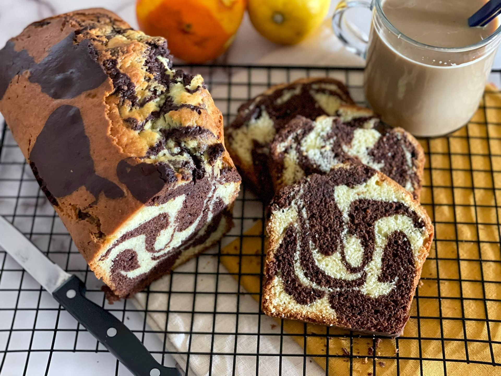Una pagnotta di torta marmorizzata è appoggiata su una griglia di raffreddamento accanto a una tazza di caffè.