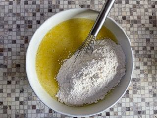Una ciotola con farina e uova e una frusta al suo interno.