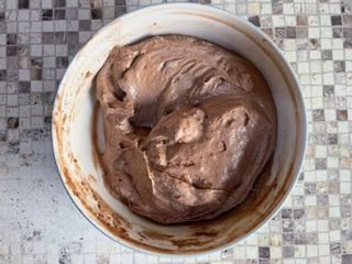 Una ciotola di glassa al cioccolato è appoggiata su un tavolo piastrellato.