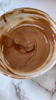 Una ciotola di salsa al cioccolato con un cucchiaio dentro su un tavolo.