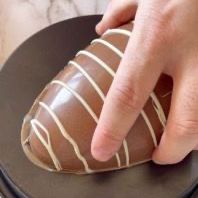 Una persona tiene in mano una fragola ricoperta di cioccolato su un piatto nero.