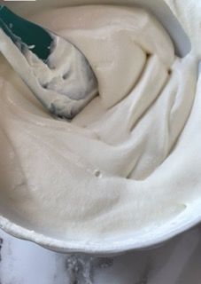 Una ciotola di glassa bianca con una spatola verde dentro.