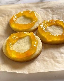 Tre biscotti con sopra della marmellata gialla sono appoggiati su un pezzo di carta.