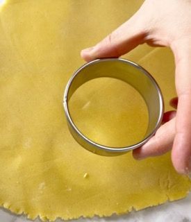 Una persona tiene in mano un tagliabiscotti sopra un pezzo di pasta