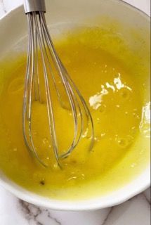 Una ciotola di liquido giallo con una frusta dentro.