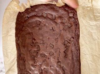 Una persona tiene in mano un pezzo di torta al cioccolato in una teglia.