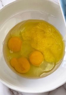 Una ciotola bianca piena di uova e olio su un tavolo.