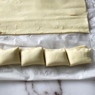 Un pezzo di pasta sfoglia viene tagliato a quadrati su un tavolo.