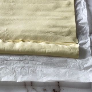 Un pezzo di pasta sfoglia è appoggiato su un foglio di carta oleata.