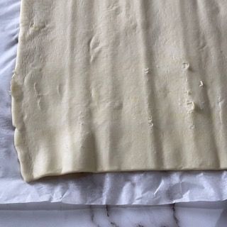 Un pezzo di pasta sfoglia è appoggiato su un foglio di carta oleata su un tavolo.