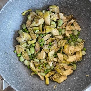 Una padella piena di carciofi piselli e altre verdure