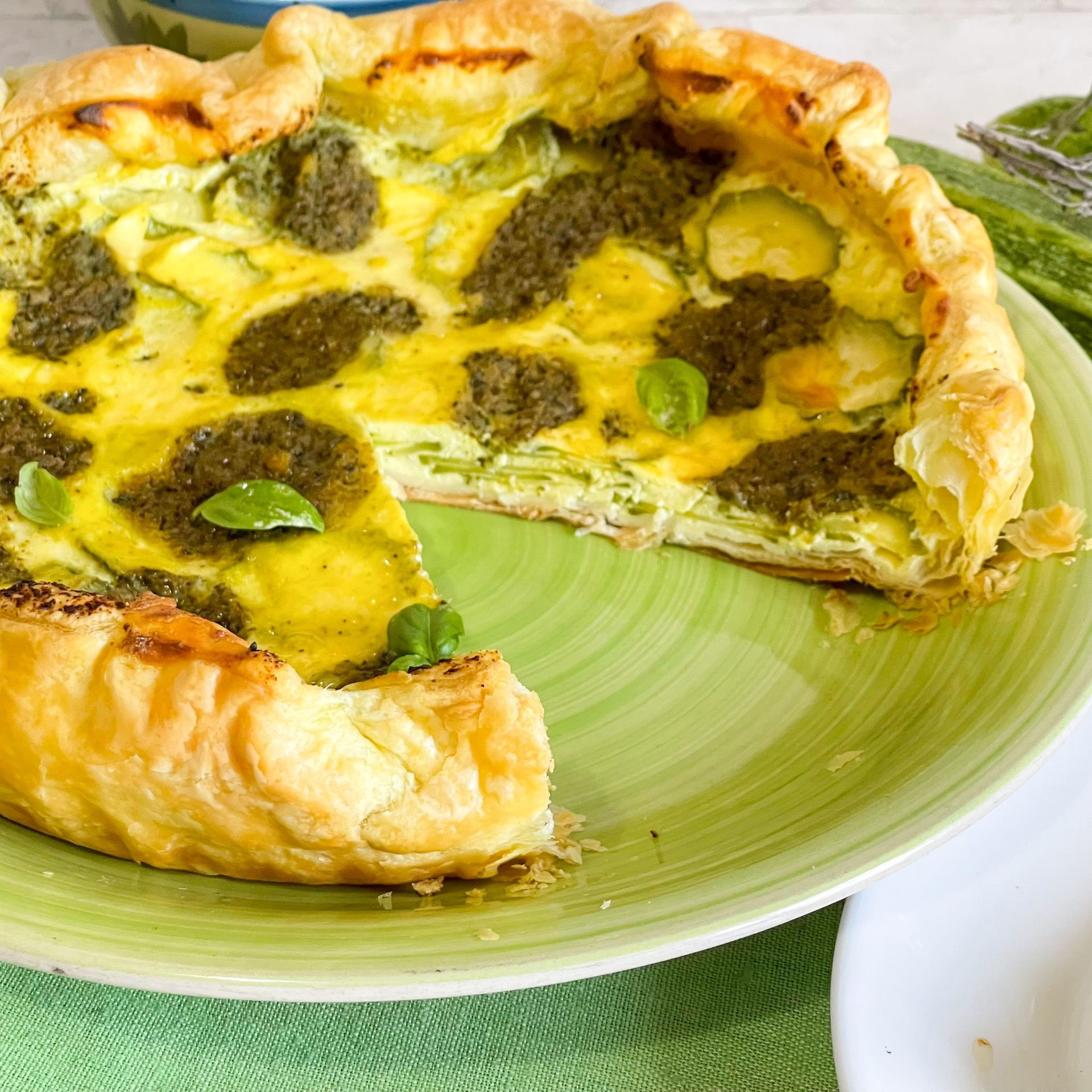 Una quiche con una fetta tolta si trova su un piatto verde.