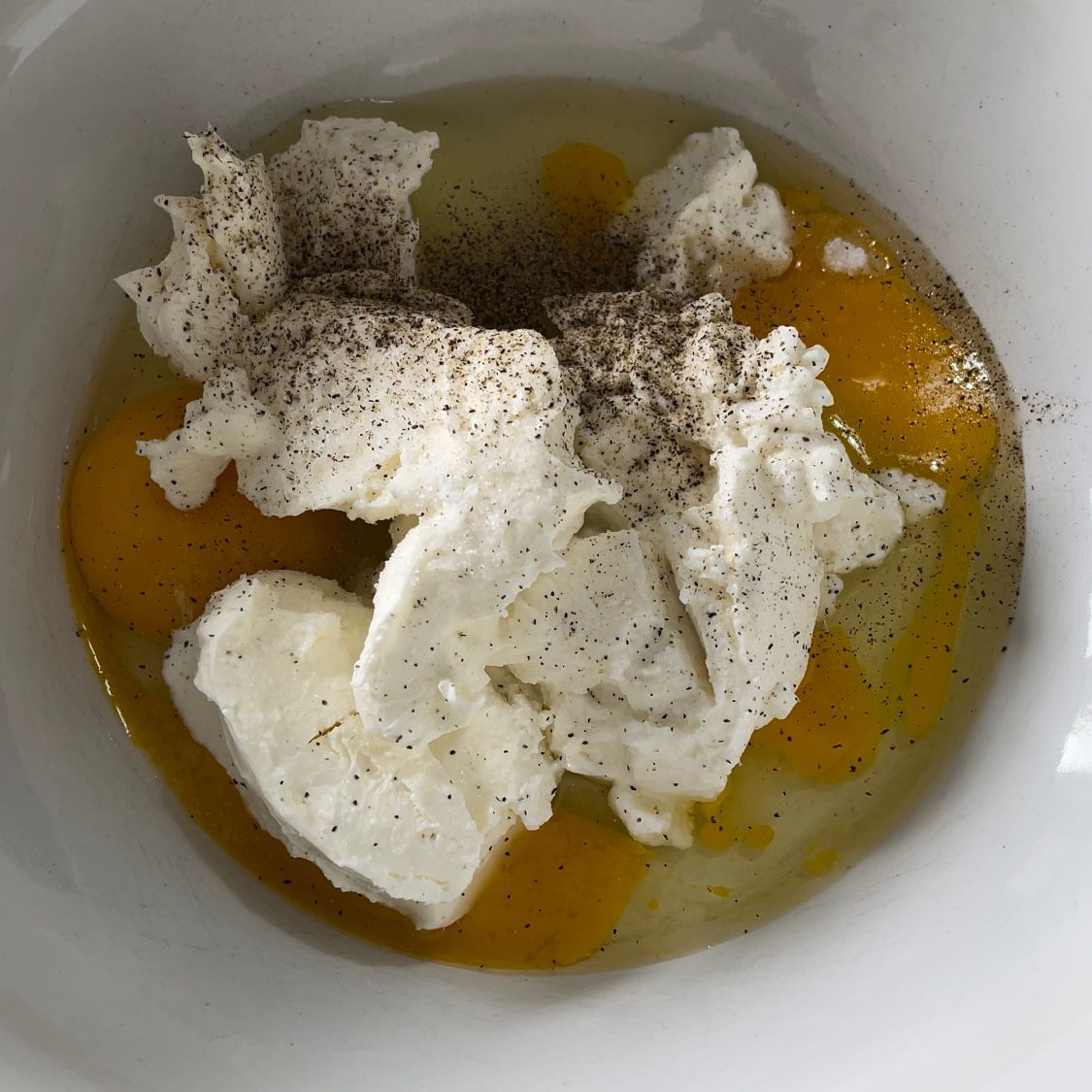 Una ciotola bianca piena di uova, formaggio e pepe