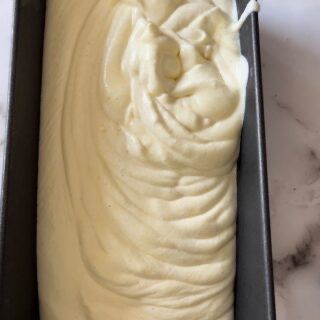 Uno stampo da plumcake pieno di glassa gialla è appoggiato su un tavolo.