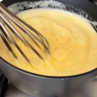 Una frusta mescola un liquido giallo in una padella