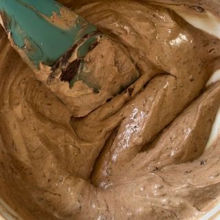 Primo piano di una ciotola di glassa al cioccolato con una spatola al suo interno.