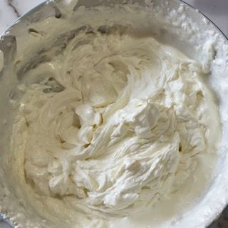 Un primo piano di una ciotola di panna montata con un cucchiaio dentro.