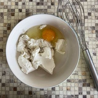 Una ciotola di uova e formaggio cremoso accanto a una frusta