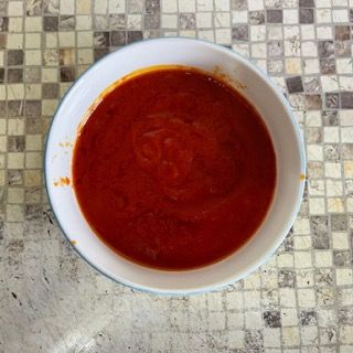 Una ciotola di salsa di pomodoro è appoggiata su un piano di lavoro piastrellato