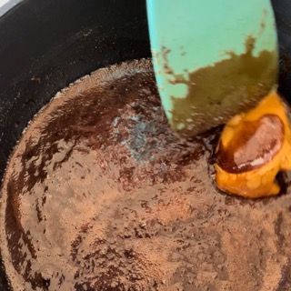 Si utilizza una spatola verde per mescolare un liquido marrone in una padella.